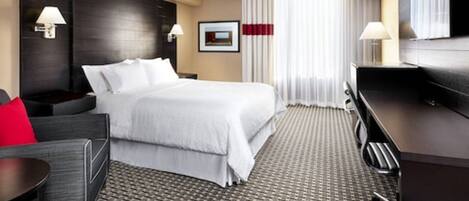 Una habitación de hotel con una cama grande, un escritorio, una silla, un televisor y un ventanal con cortinas.