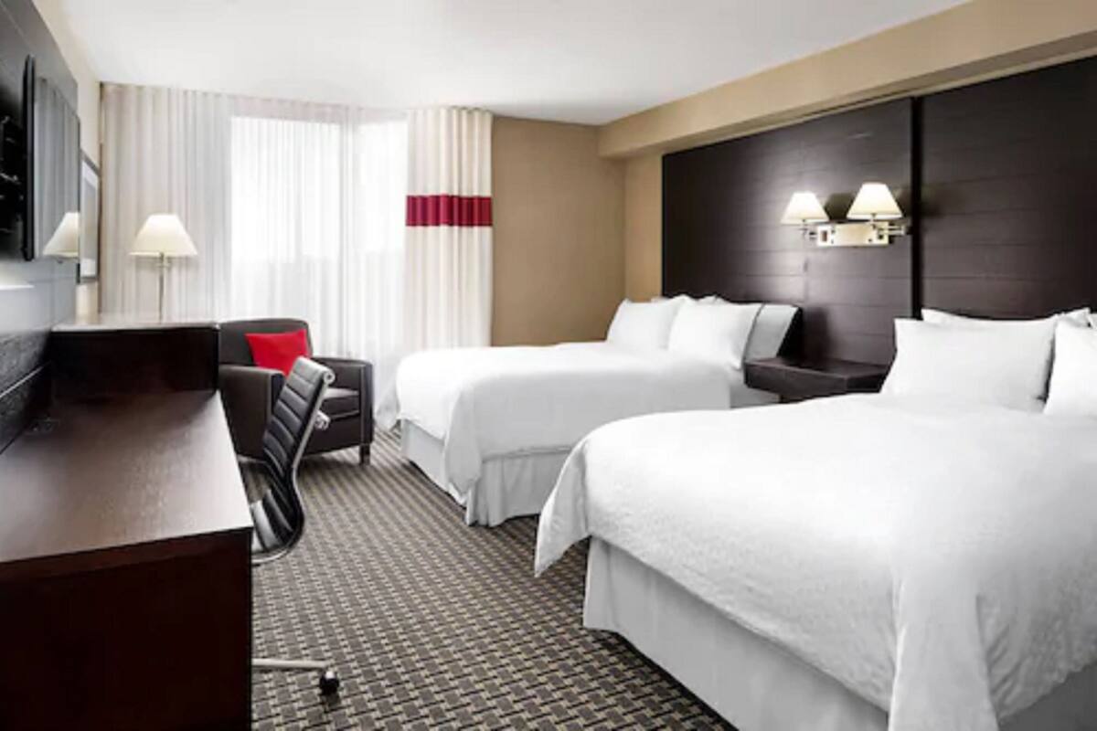 A hotel room with two beds, a desk, a chair, and a TV.