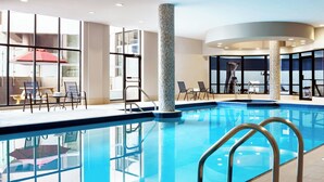 Una piscina interior con paredes de vidrio transparente, barandillas metálicas y vistas al exterior.