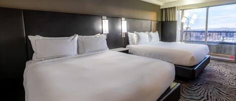 Une chambre d’hôtel avec deux lits, une grande fenêtre donnant sur la ville et un tapis à motifs zébrés.