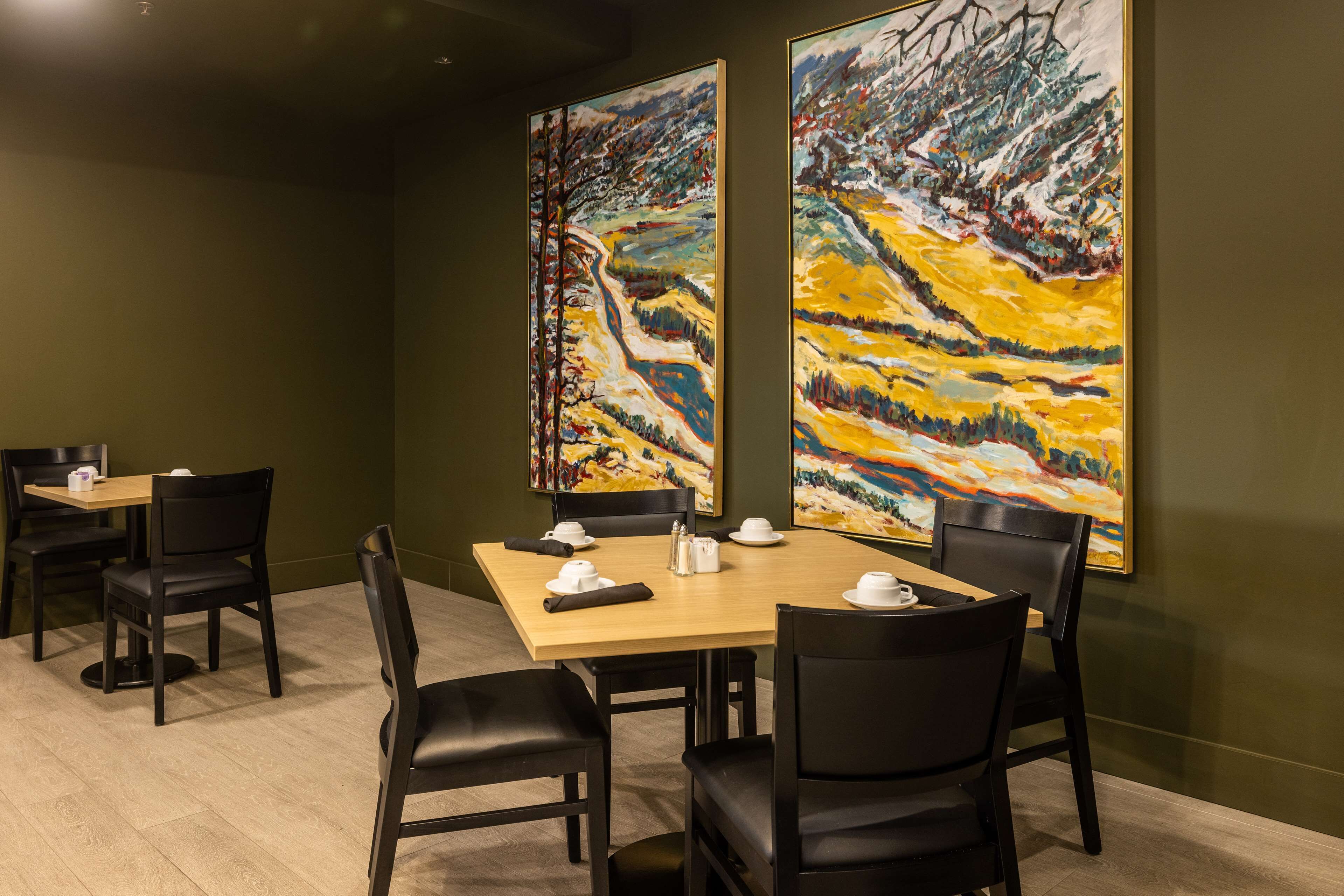 A conference room with a wooden table, black chairs, and two large abstract paintings on the walls.