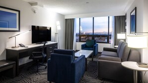 A hotel room with a desk, a television, a sofa, and a view of the city. - DoubleTree by Hilton Calgary North (Calgary)