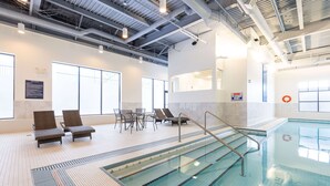 A swimming pool with lounge chairs and a table, surrounded by large windows and a tiled floor. - DoubleTree by Hilton Calgary North (Calgary)