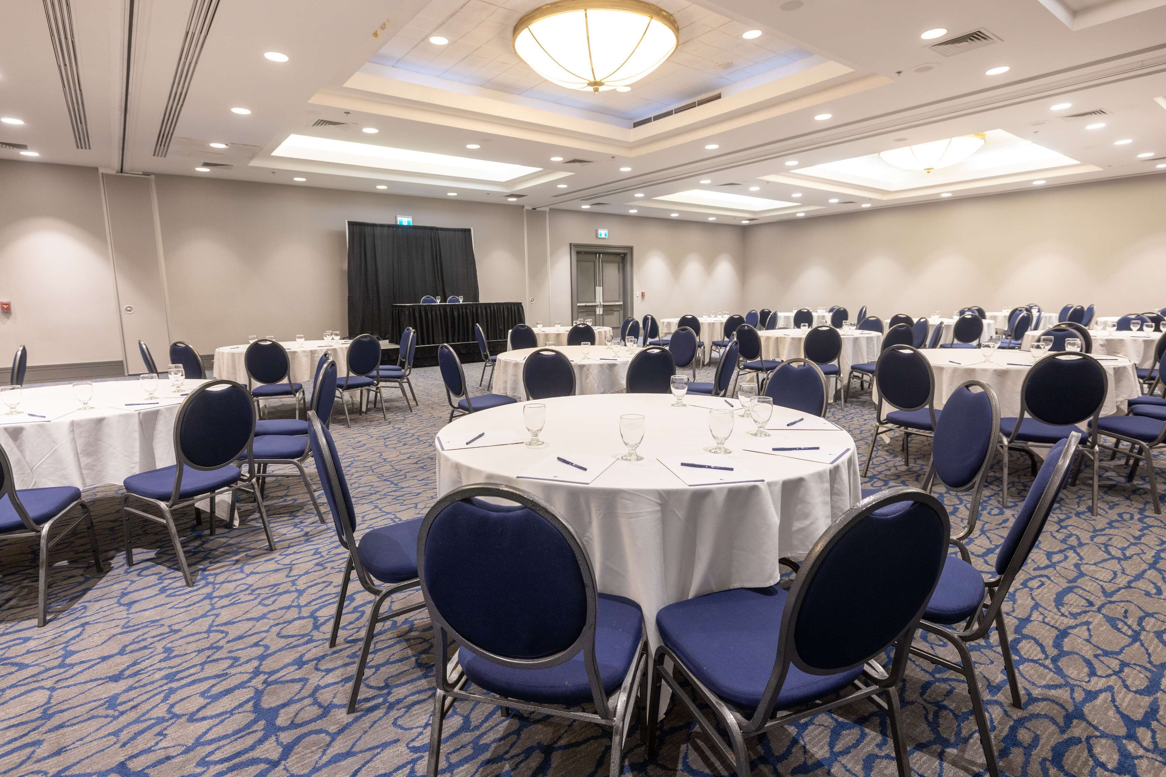 Une salle de conférence avec des tables rondes, des chaises bleues et des nappes blanches.