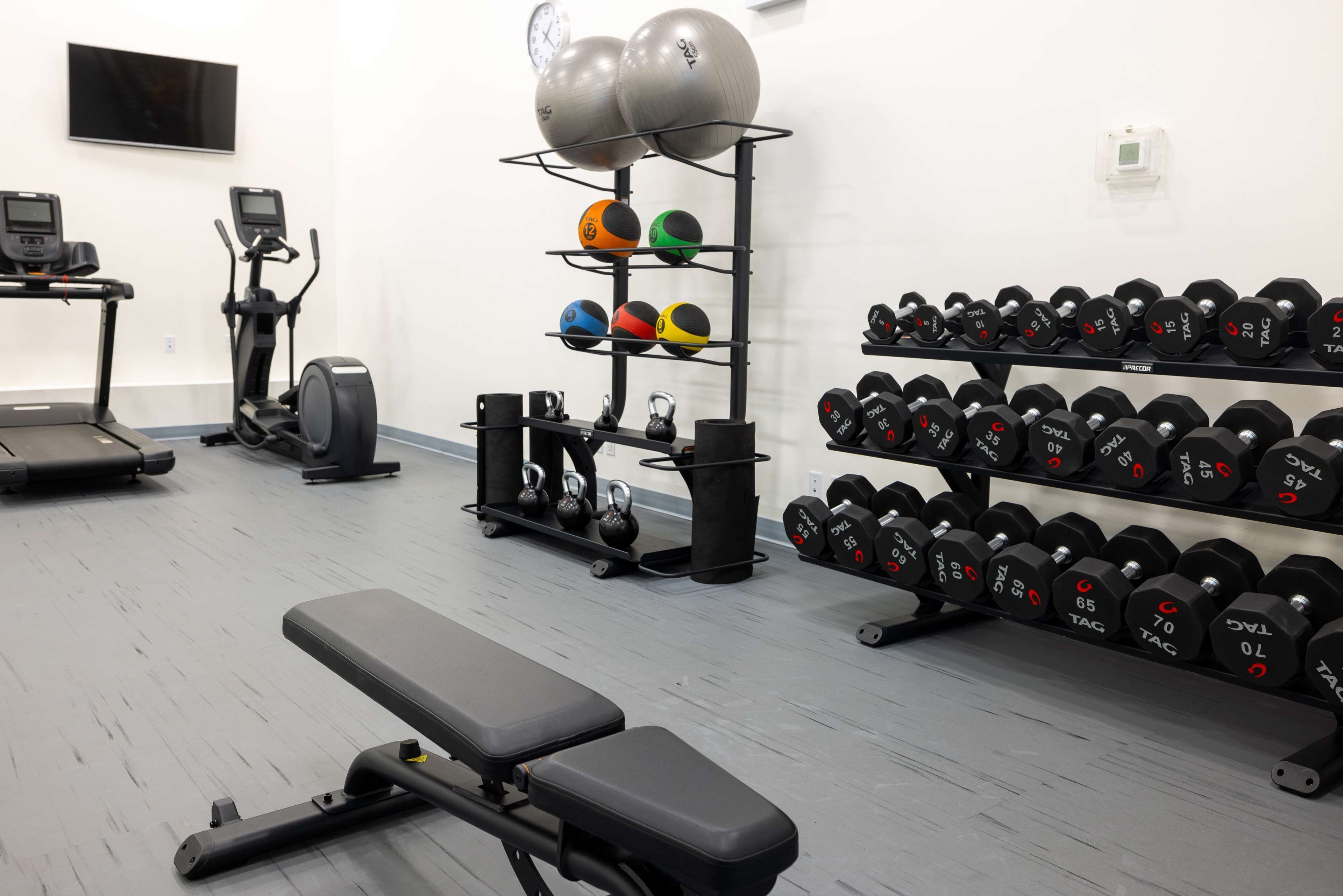 A gym with exercise equipment, including treadmills, an elliptical, kettlebells, and a rack of dumbbells.