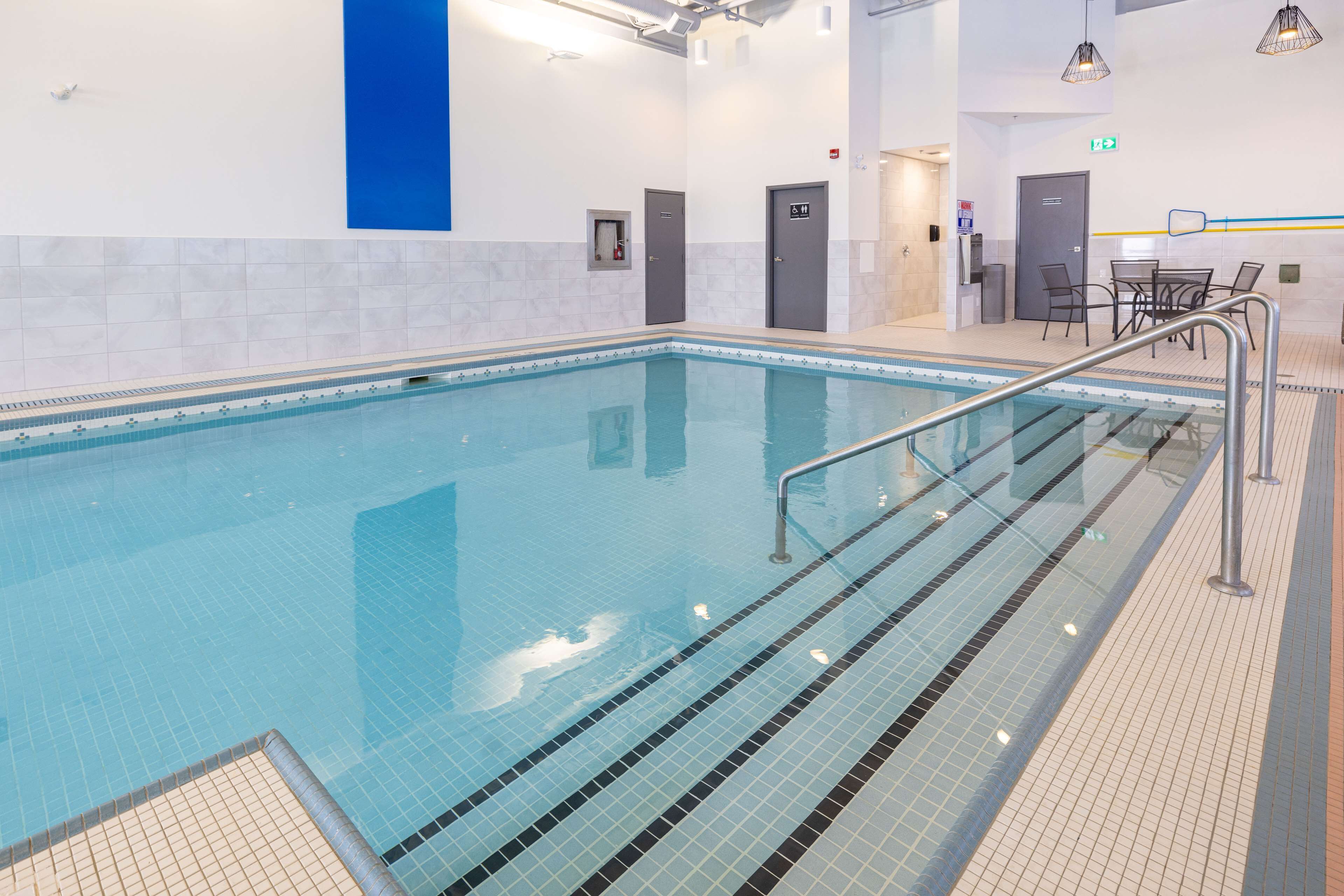 Une piscine dotée d’une terrasse carrelée, d’un vestiaire et d’un espace détente avec des tables et des chaises.