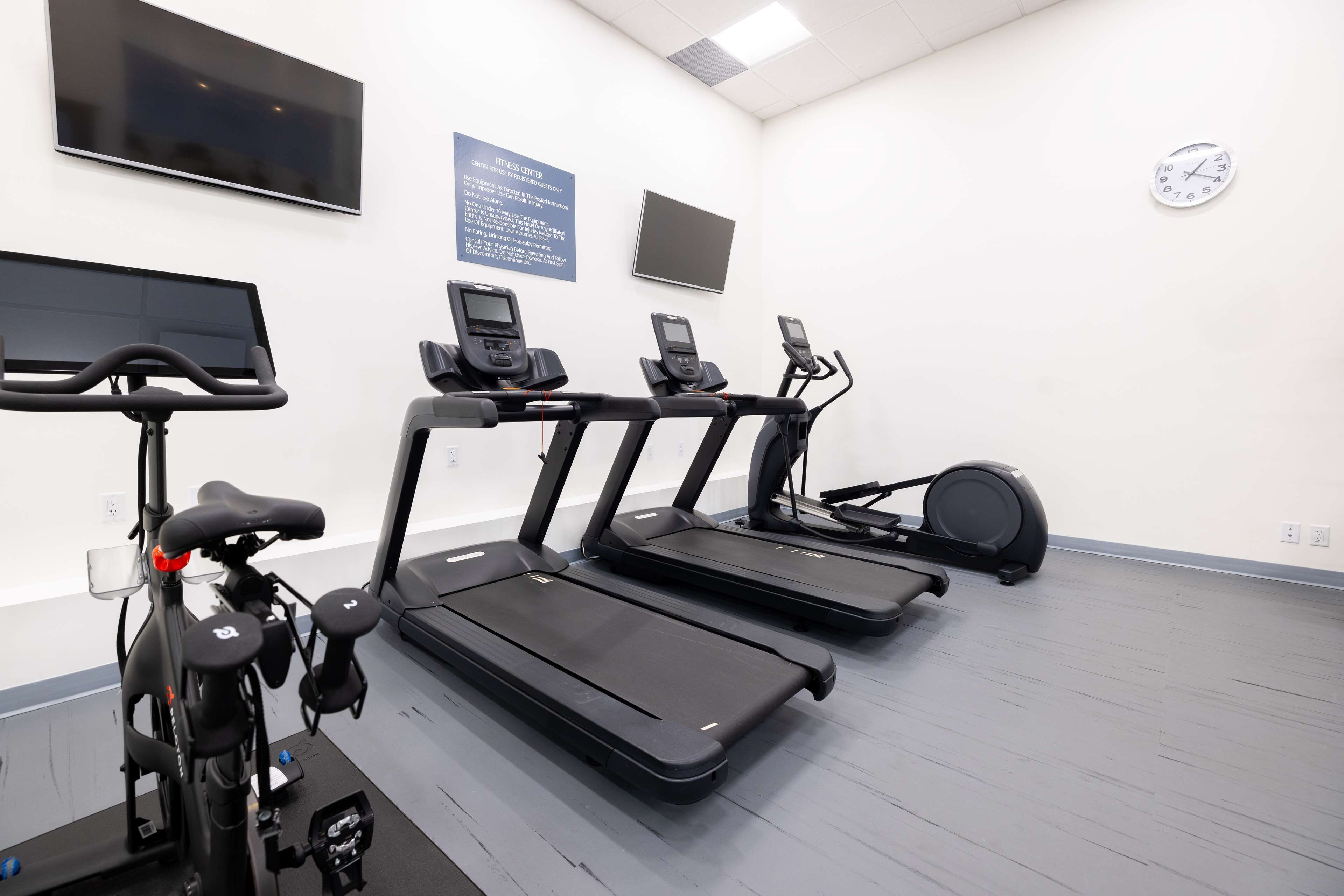 Un gimnasio con cintas de correr, una bicicleta estática y un televisor montado en la pared.