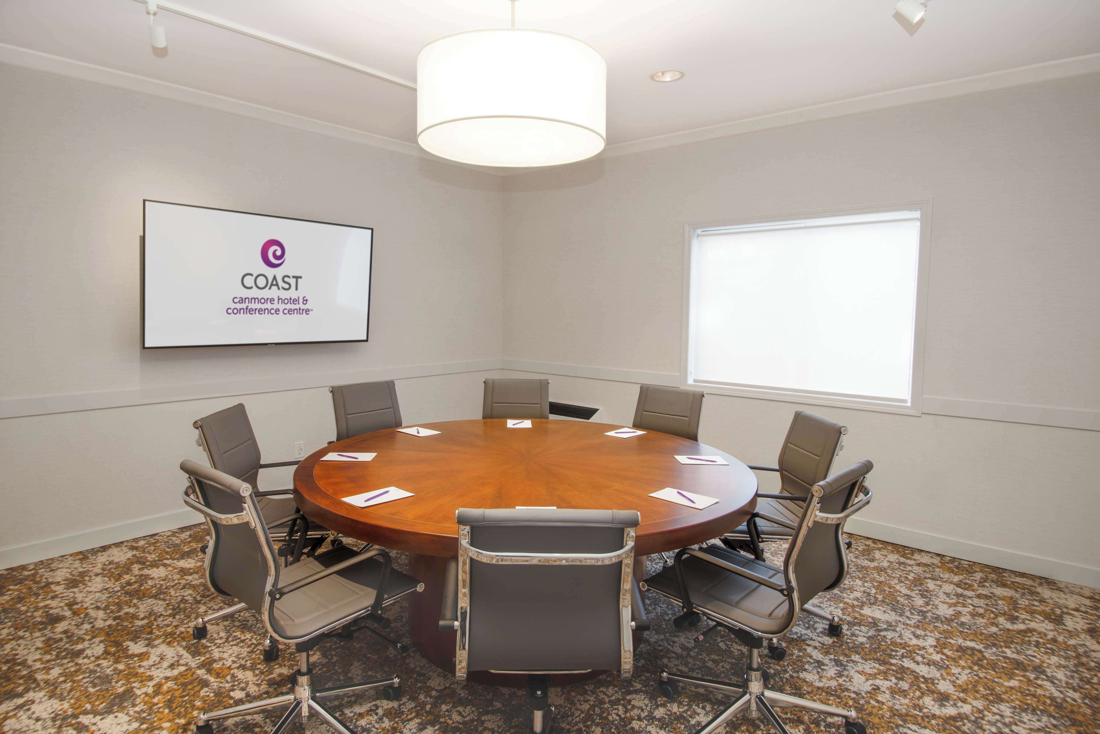 A conference room with a round table, six chairs, a large window, and a sign on the wall.