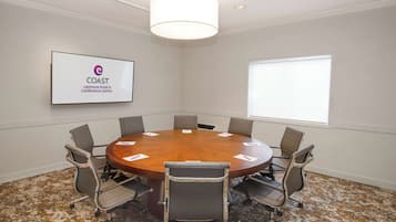 A conference room with a round table, six chairs, a large window, and a sign on the wall.