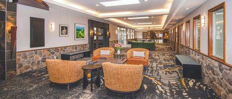 A hotel lobby with a stone wall, a reception desk, and a seating area with wicker chairs and a coffee table.