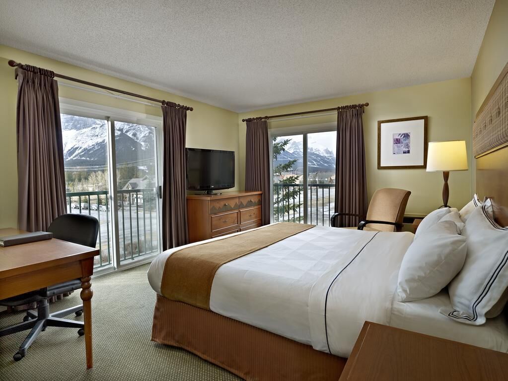Une chambre d’hôtel équipée d’un lit, d’un bureau, d’une chaise, d’une télévision et d’un balcon avec vue sur la montagne.