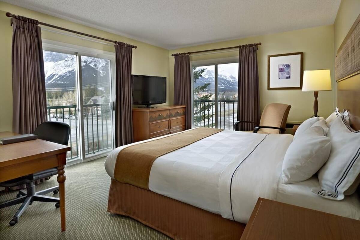 Ein Hotelzimmer mit Bett, Schreibtisch, Stuhl, Fernseher und einem Balkon mit Blick auf die Berge.