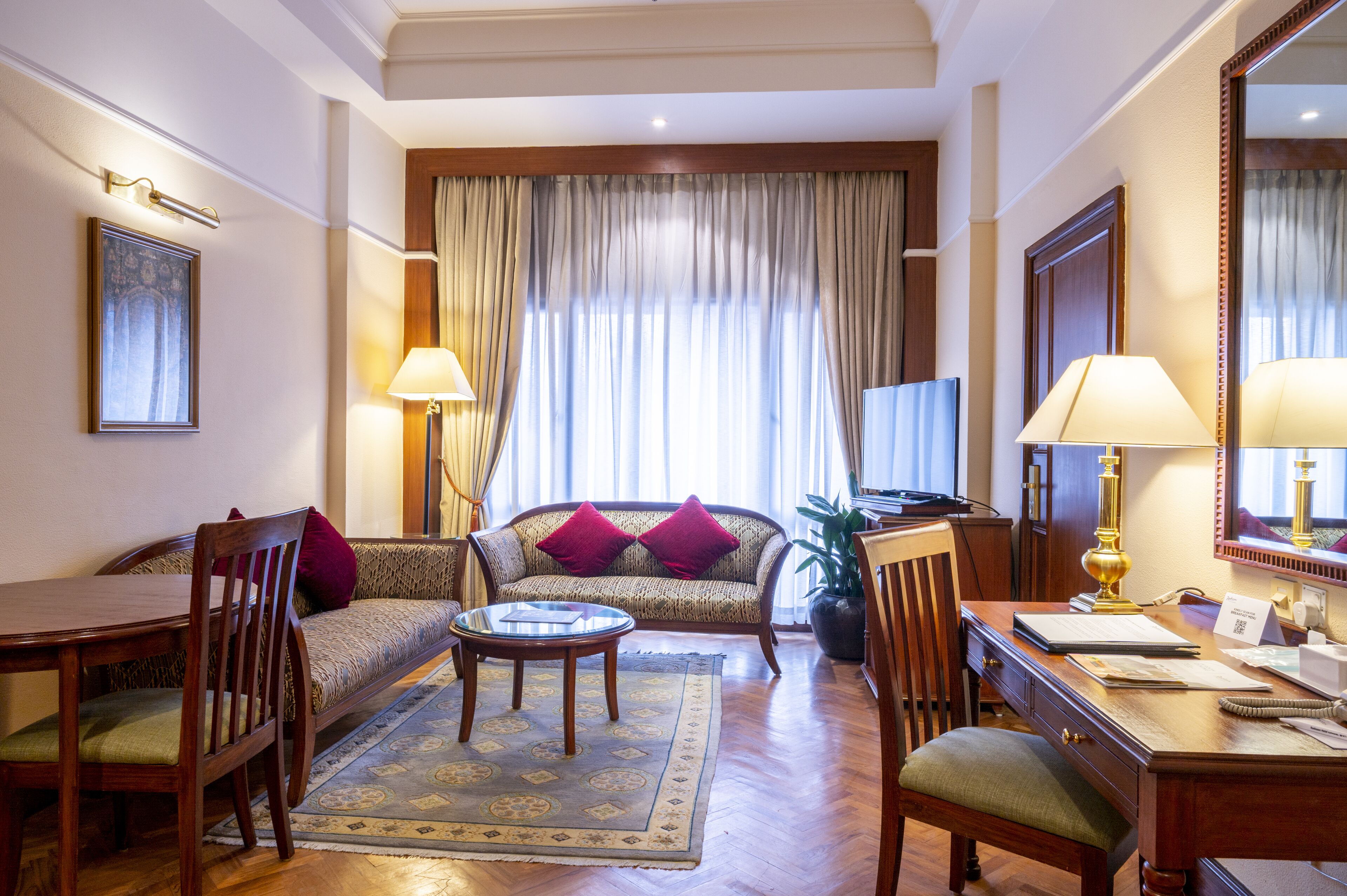 Une chambre d’hôtel équipée d’un canapé, d’une table à manger, d’une table basse, d’un bureau avec une lampe et d’un téléviseur.