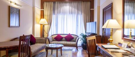 Une chambre d’hôtel équipée d’un canapé, d’une table à manger, d’une table basse, d’un bureau avec une lampe et d’un téléviseur.