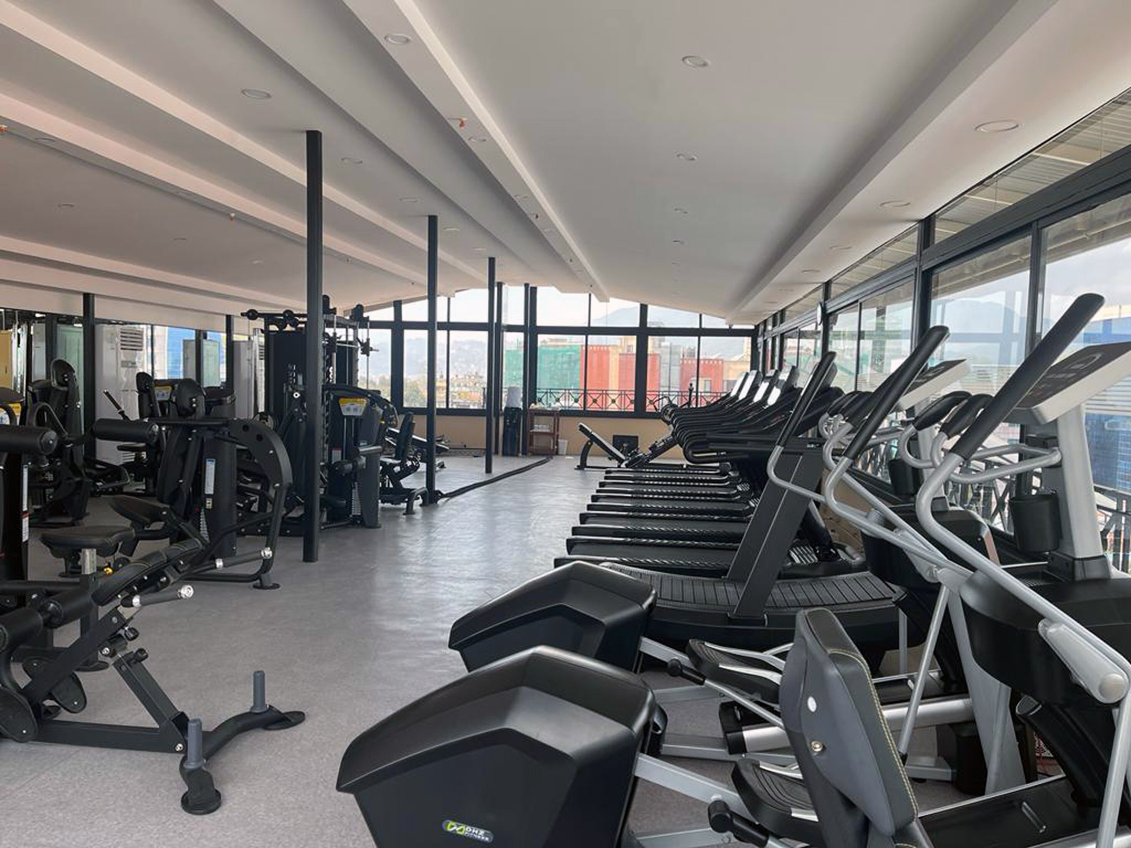 A modern gym with treadmills, weight machines, and large windows offering city views.