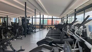 A modern gym with treadmills, weight machines, and large windows offering city views.