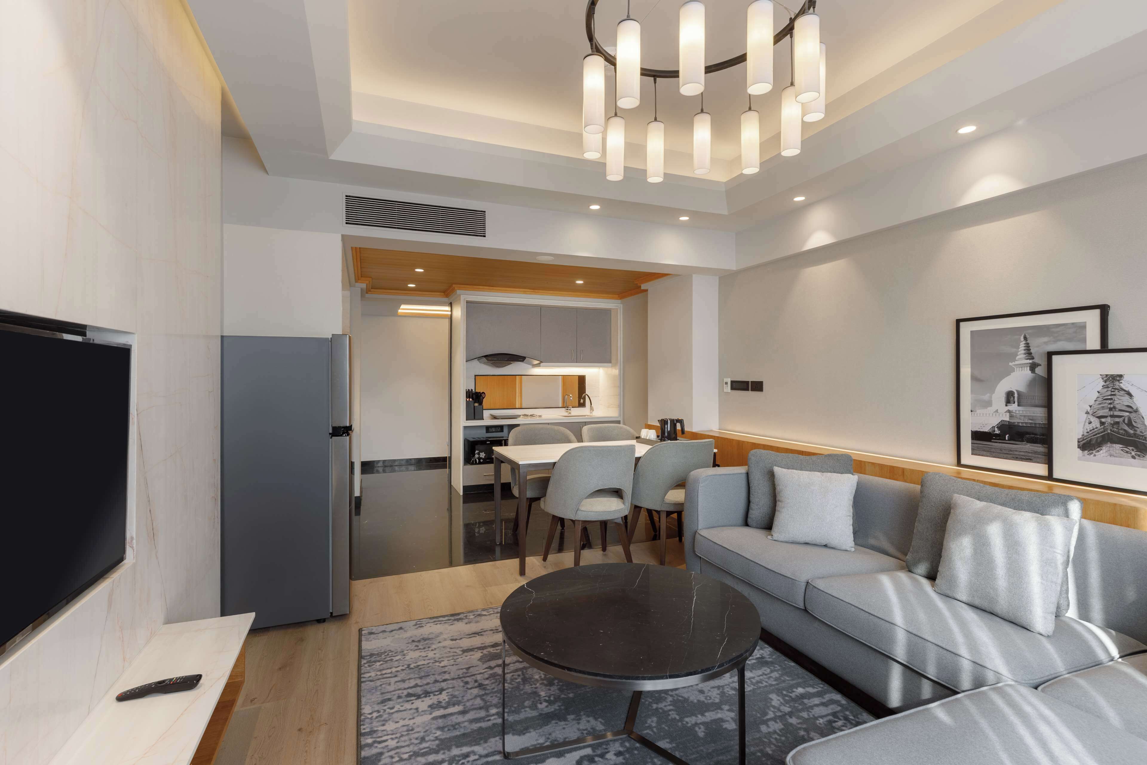 A modern living room with a sofa, a coffee table, and a TV. There is a kitchen area visible in the background.