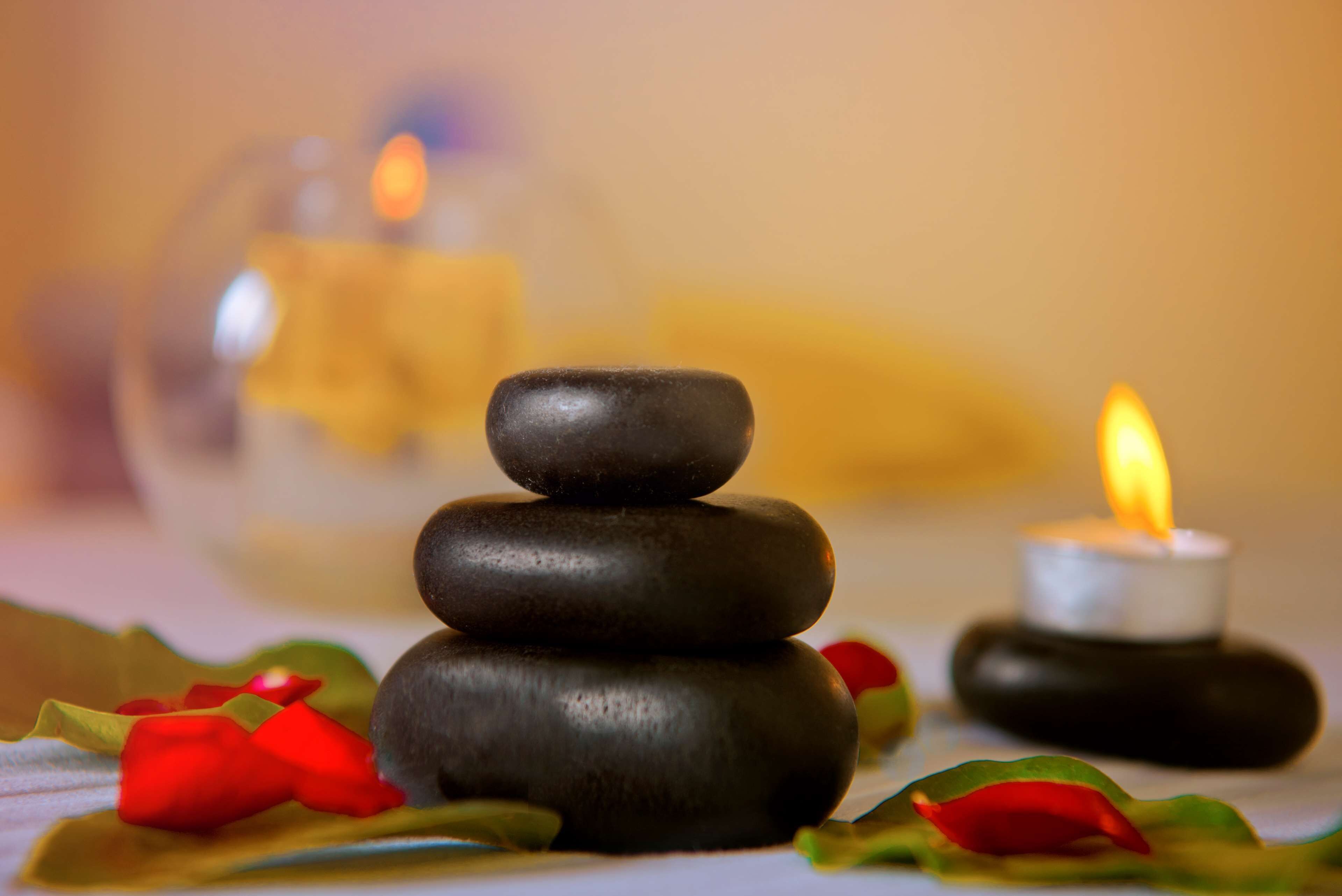 A stack of smooth, dark stones with a lit candle beside them, surrounded by red and green leaves.