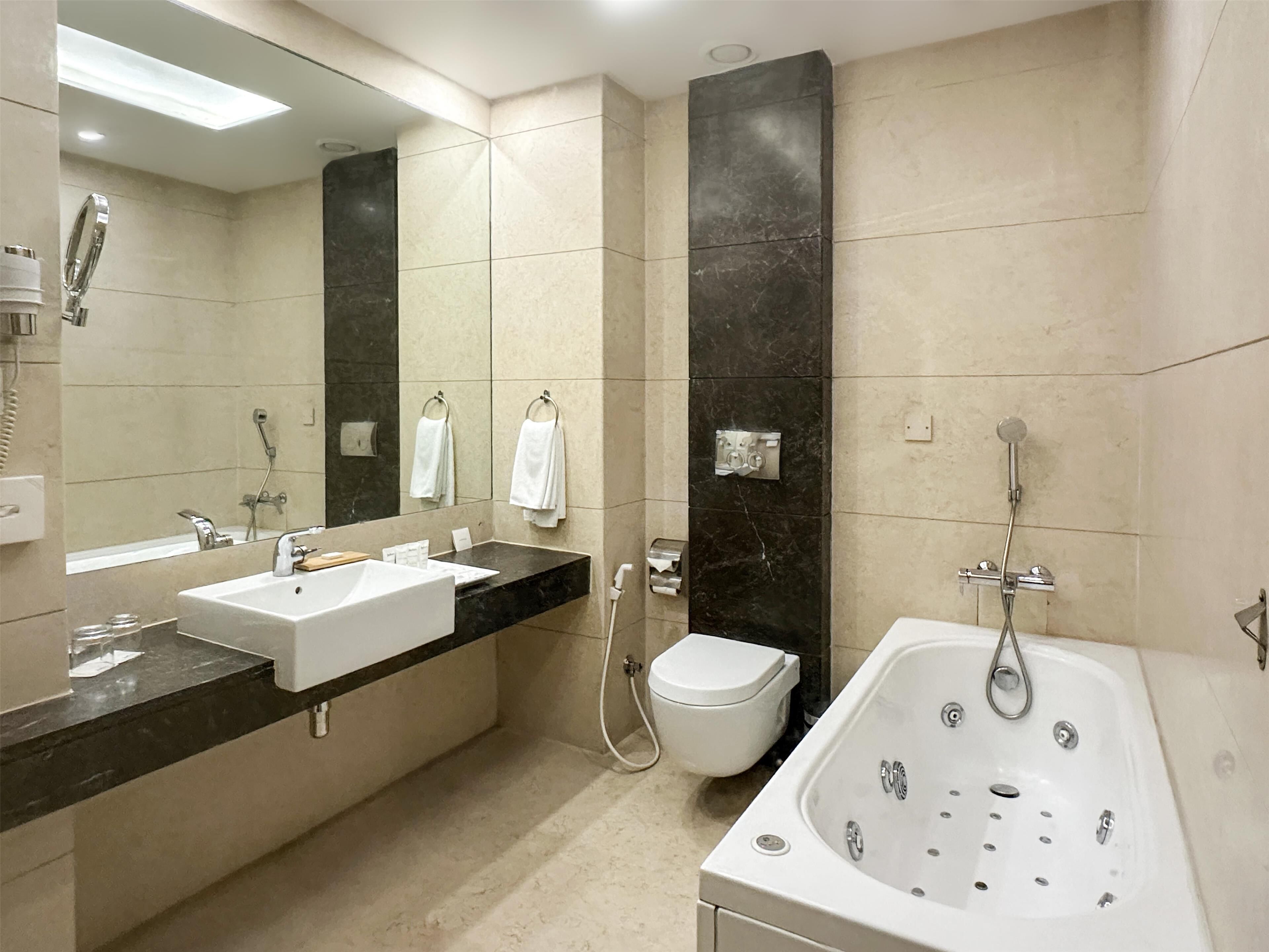 A modern bathroom with a large mirror, a white sink, a bathtub, and a toilet.