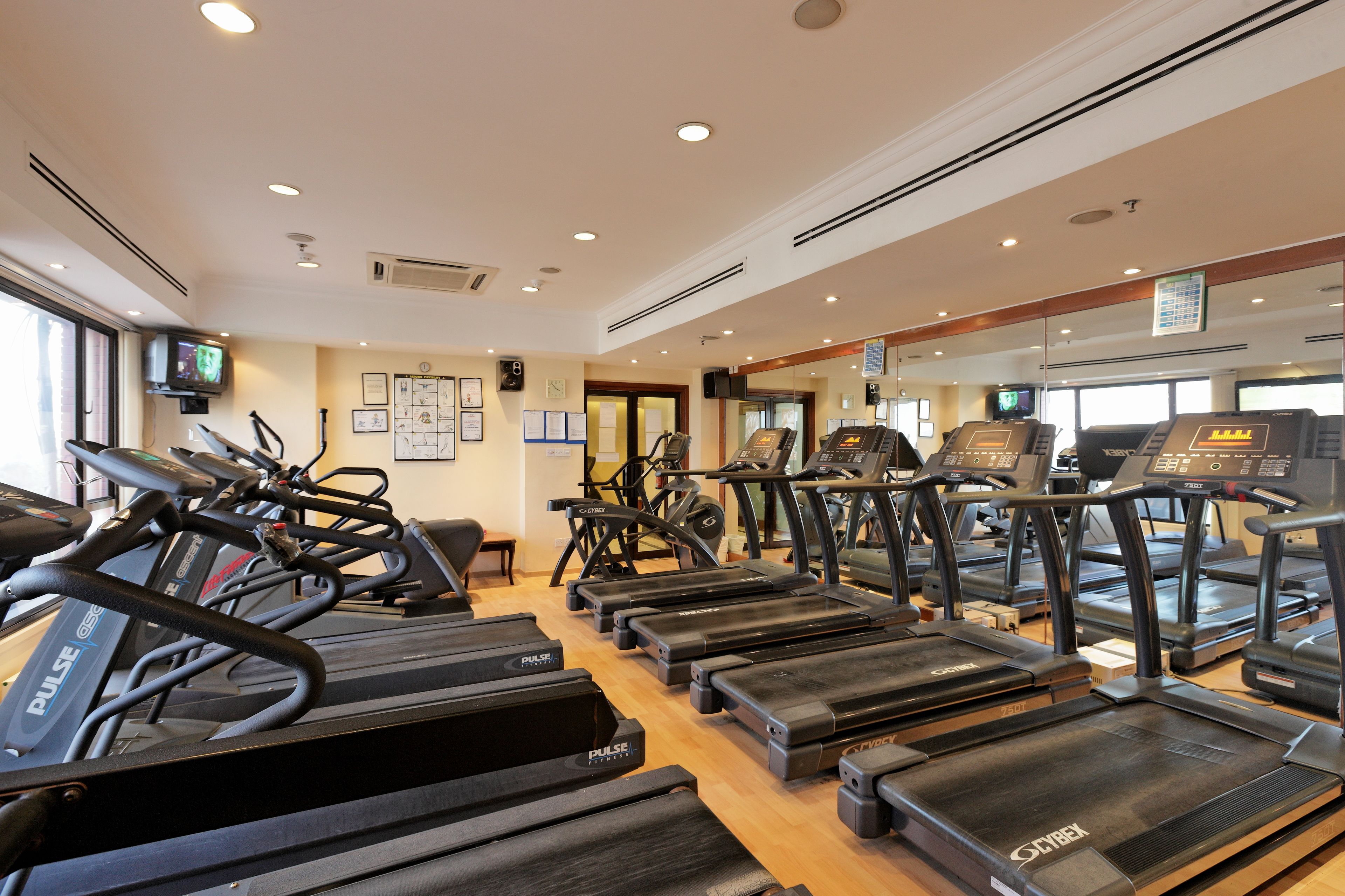 Une salle de sport équipée de plusieurs tapis de course, de vélos d’exercice et d’un téléviseur fixé au mur.