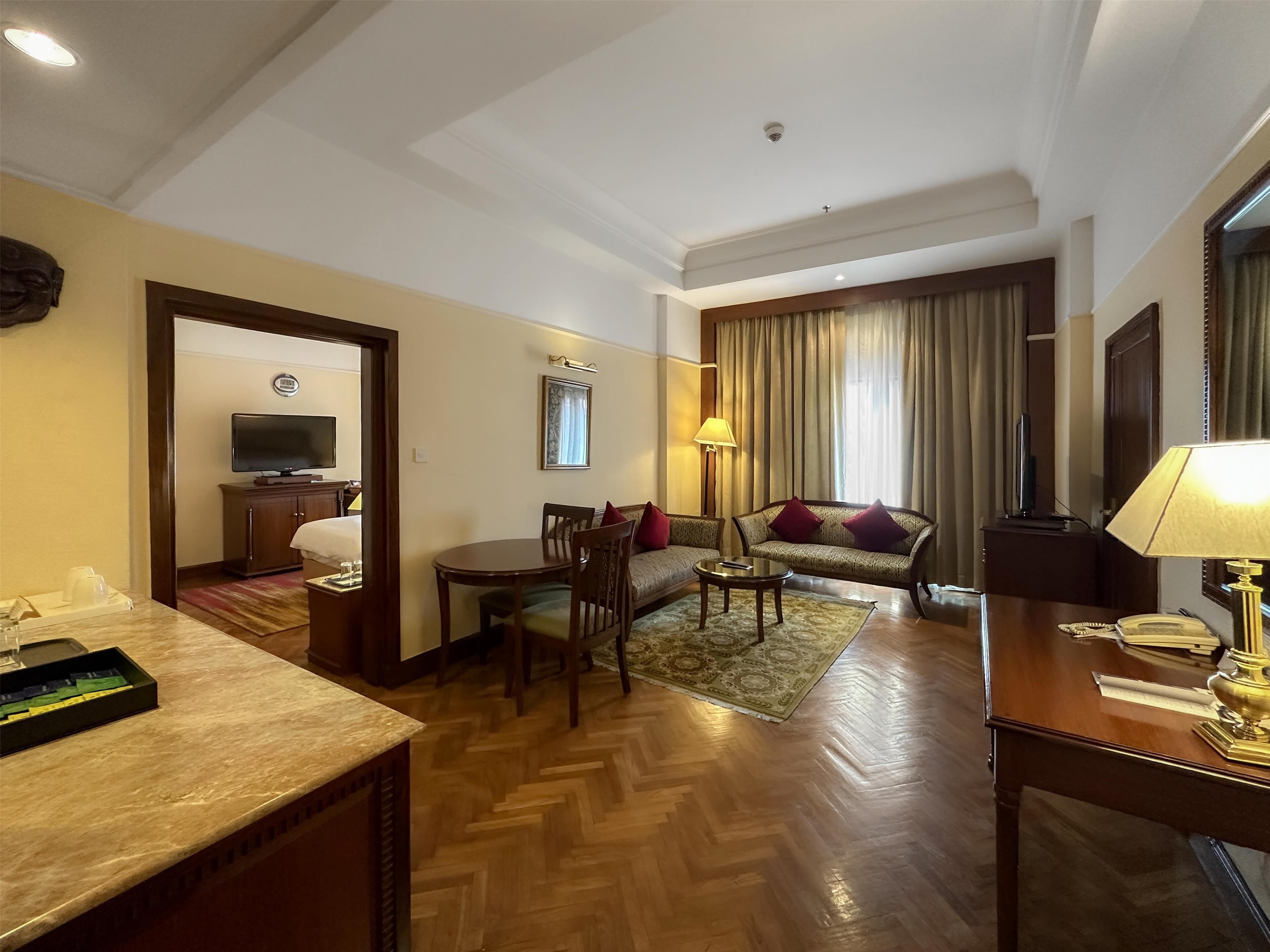 A hotel room with a dining area, a sofa, a TV, and a lamp.