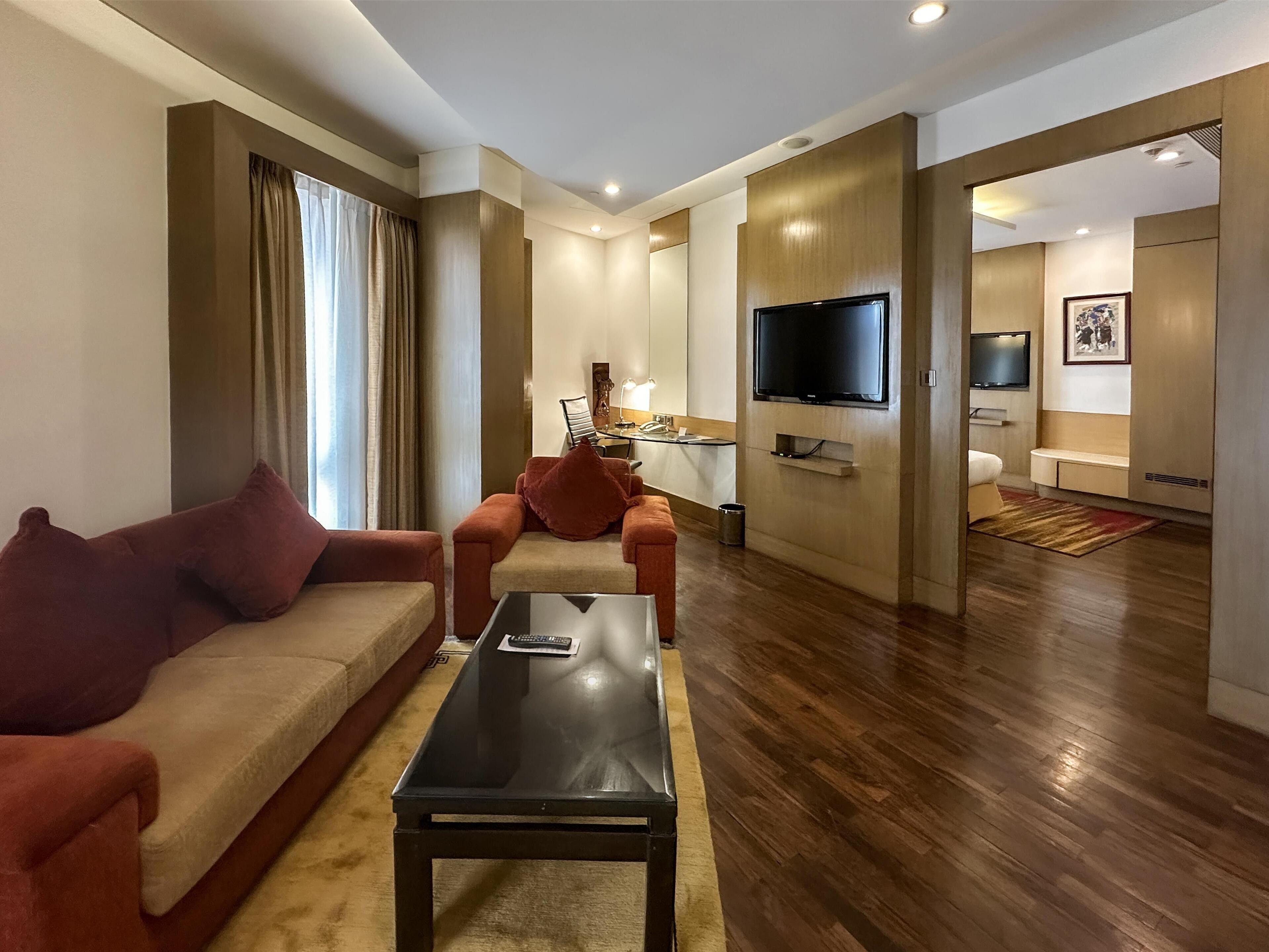 A modern hotel room with a living area featuring a sofa, a coffee table, and a TV mounted on the wall.