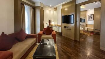 A modern hotel room with a living area featuring a sofa, a coffee table, and a TV mounted on the wall.