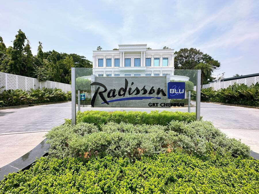 A sign for Radisson GRT Chennai with a modern building in the background.
