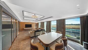 Una habitación de hotel moderna con una gran mesa de comedor, asientos cómodos, una zona de cocina y vistas a una pista de carreras.