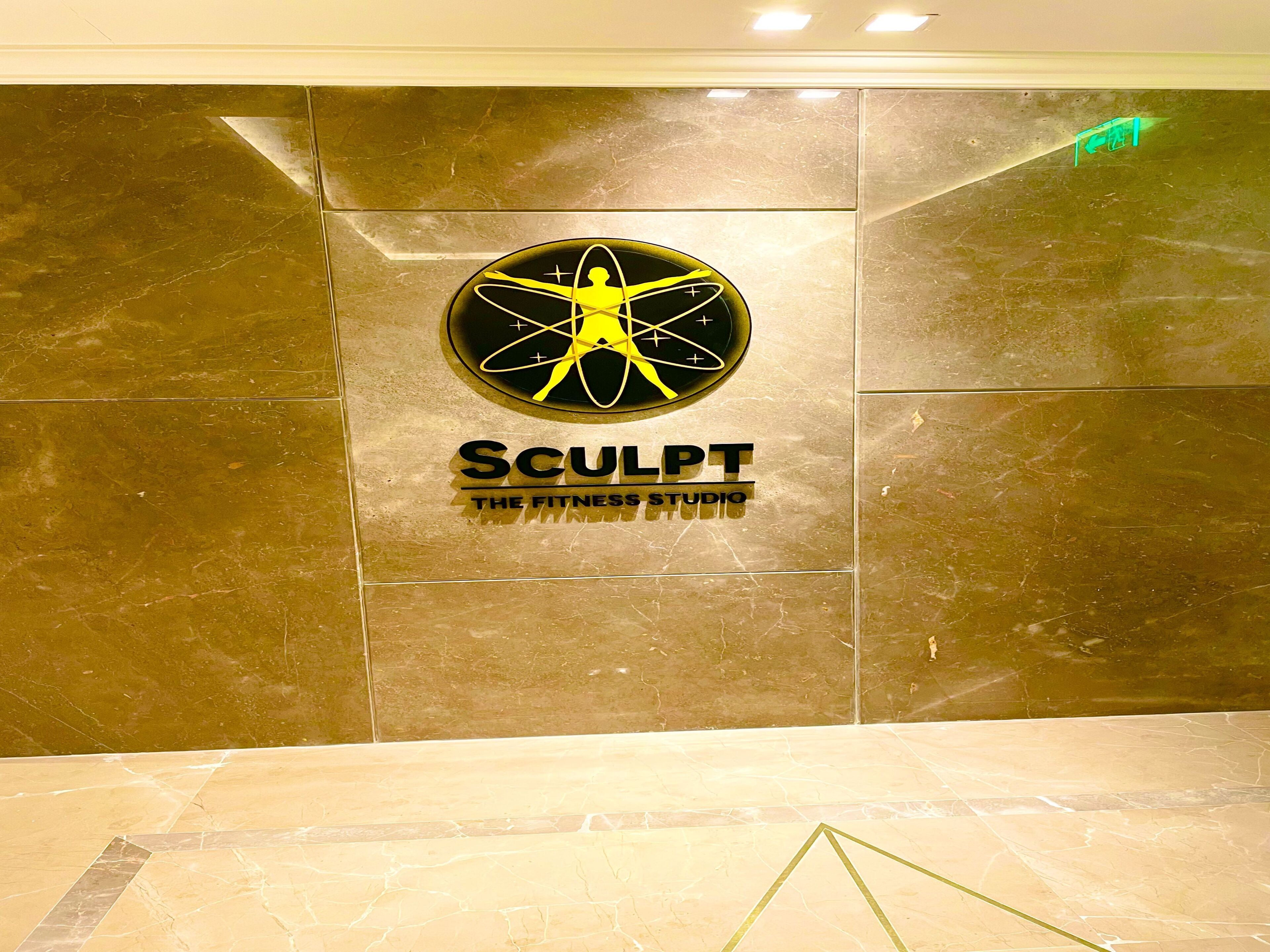 Un logo représentant une silhouette humaine stylisée, accompagné du texte « Sculpt The Fitness Studio », sur un mur de marbre.