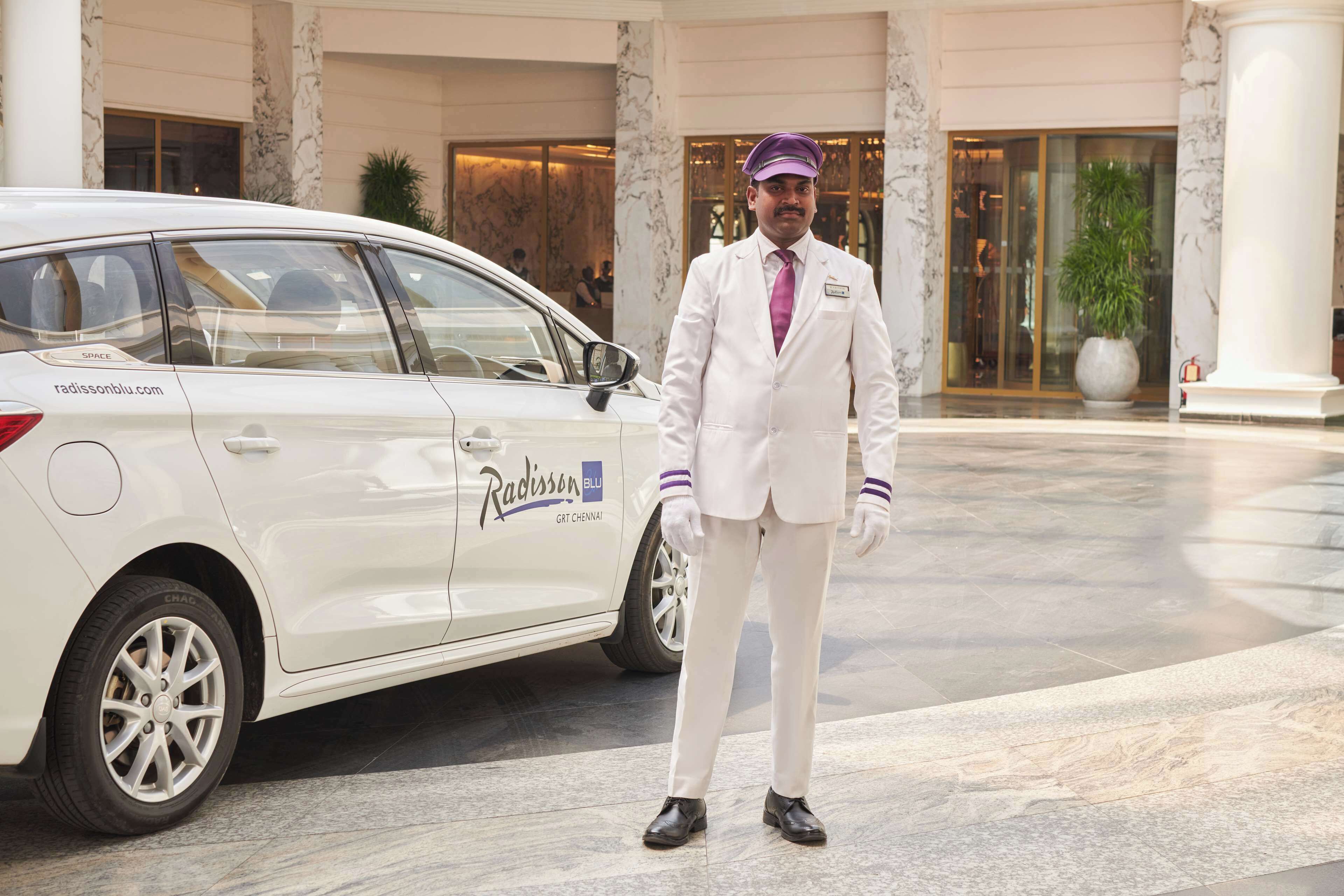 Un coche blanco de Radisson BLU estacionado frente a un hotel con columnas de mármol y una planta grande en maceta.