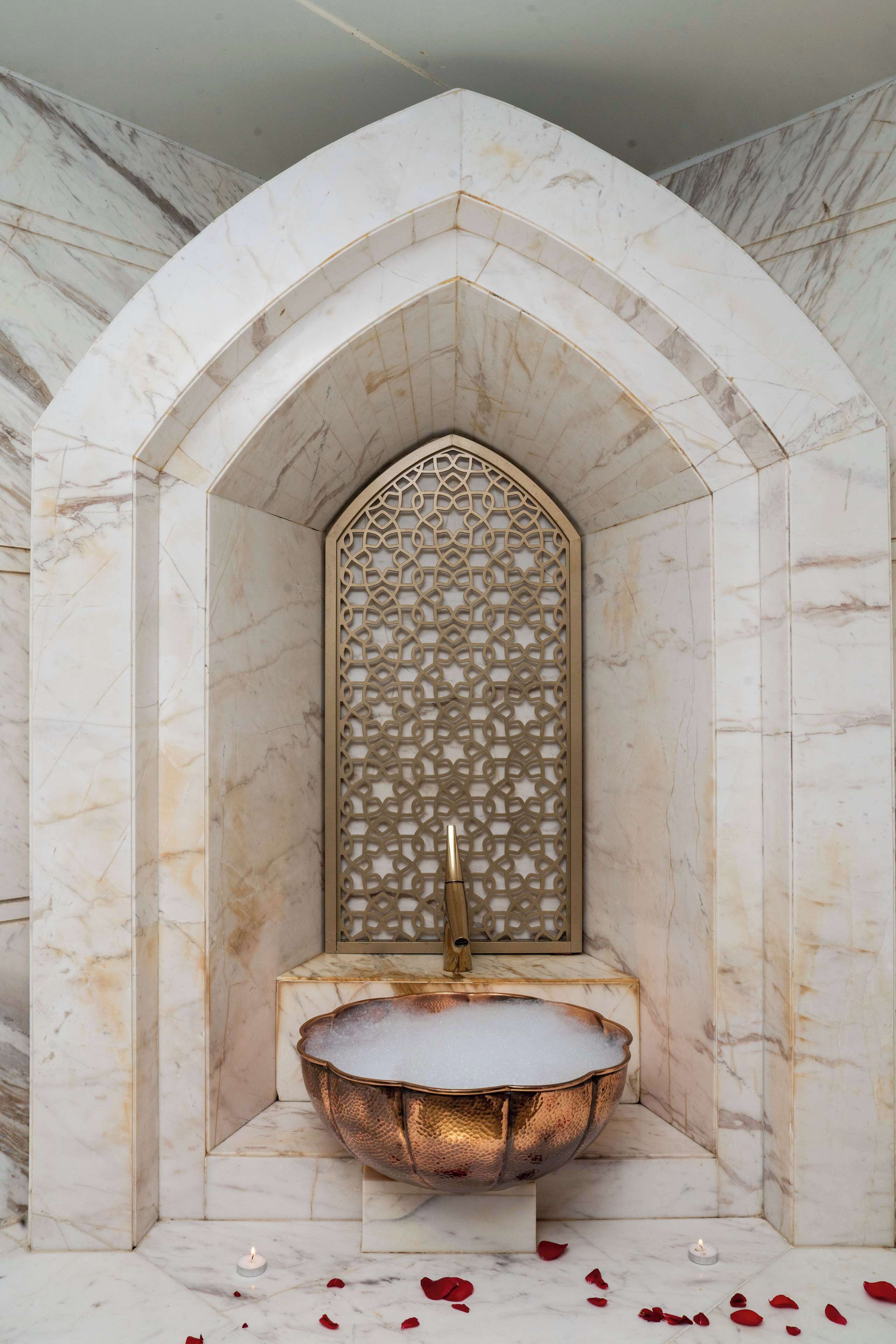 A marble-walled alcove with a decorative screen, a golden basin, and a candle.