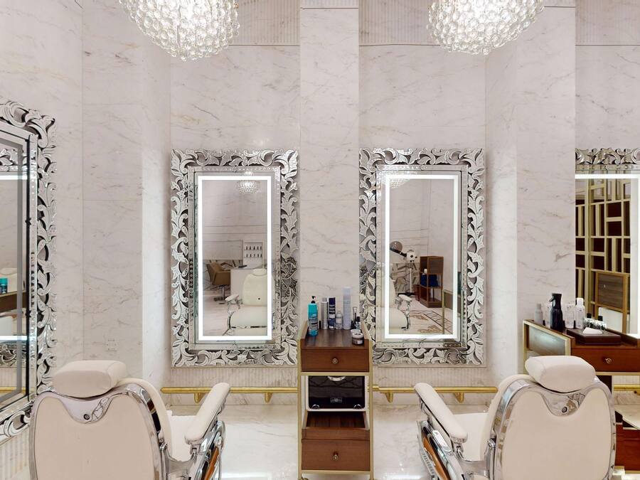 A luxurious bathroom with three large mirrors, marble walls, and a vanity with a gold bar.