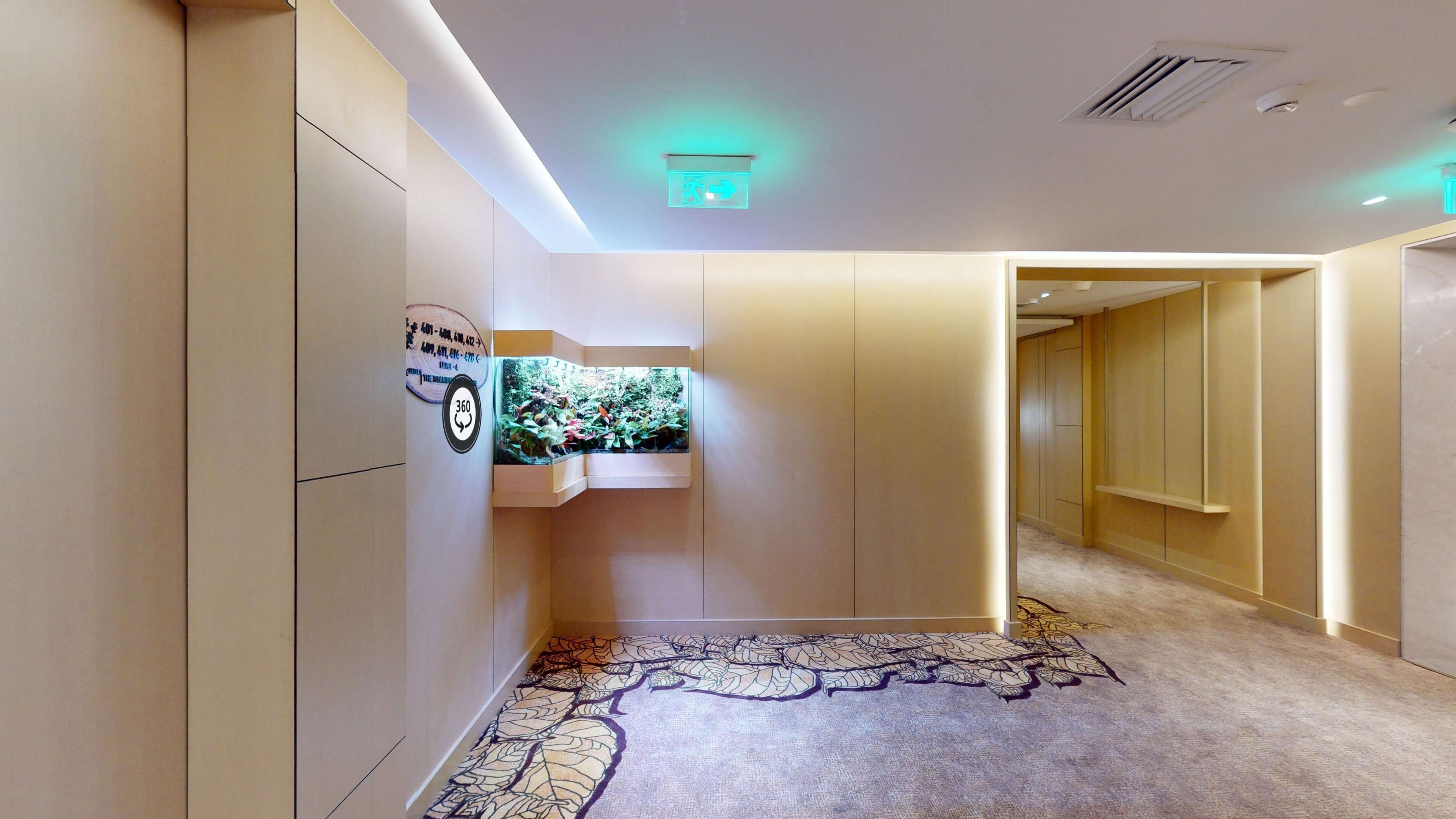 A hallway with a patterned carpet, a wall-mounted aquarium, and a sign with a phone number.