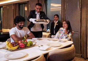 A dining area with a table set for four people, a waiter serving food, and a buffet with fruits and vegetables. - Radisson Blu Hotel & Suites GRT Chennai (Chennai)