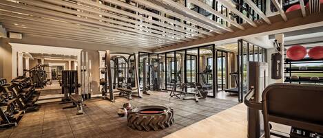 Une salle de sport équipée de divers appareils d’exercice, dotée d’un plancher en bois et d’un plafond avec des poutres apparentes.
