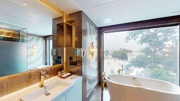 Un baño moderno con un espejo grande, dos lavamanos, una bañera y vistas a la ciudad a través de amplias ventanas.