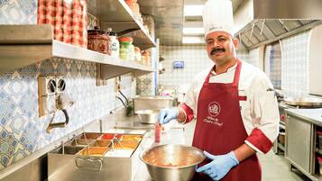 Um chef em uma cozinha com eletrodomésticos de aço inoxidável, painel de azulejos e prateleiras com potes e recipientes.