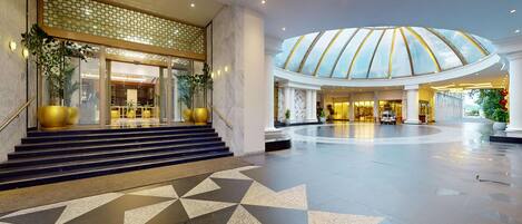 A spacious lobby with a geometric tile floor, a grand staircase, and a large glass dome ceiling.