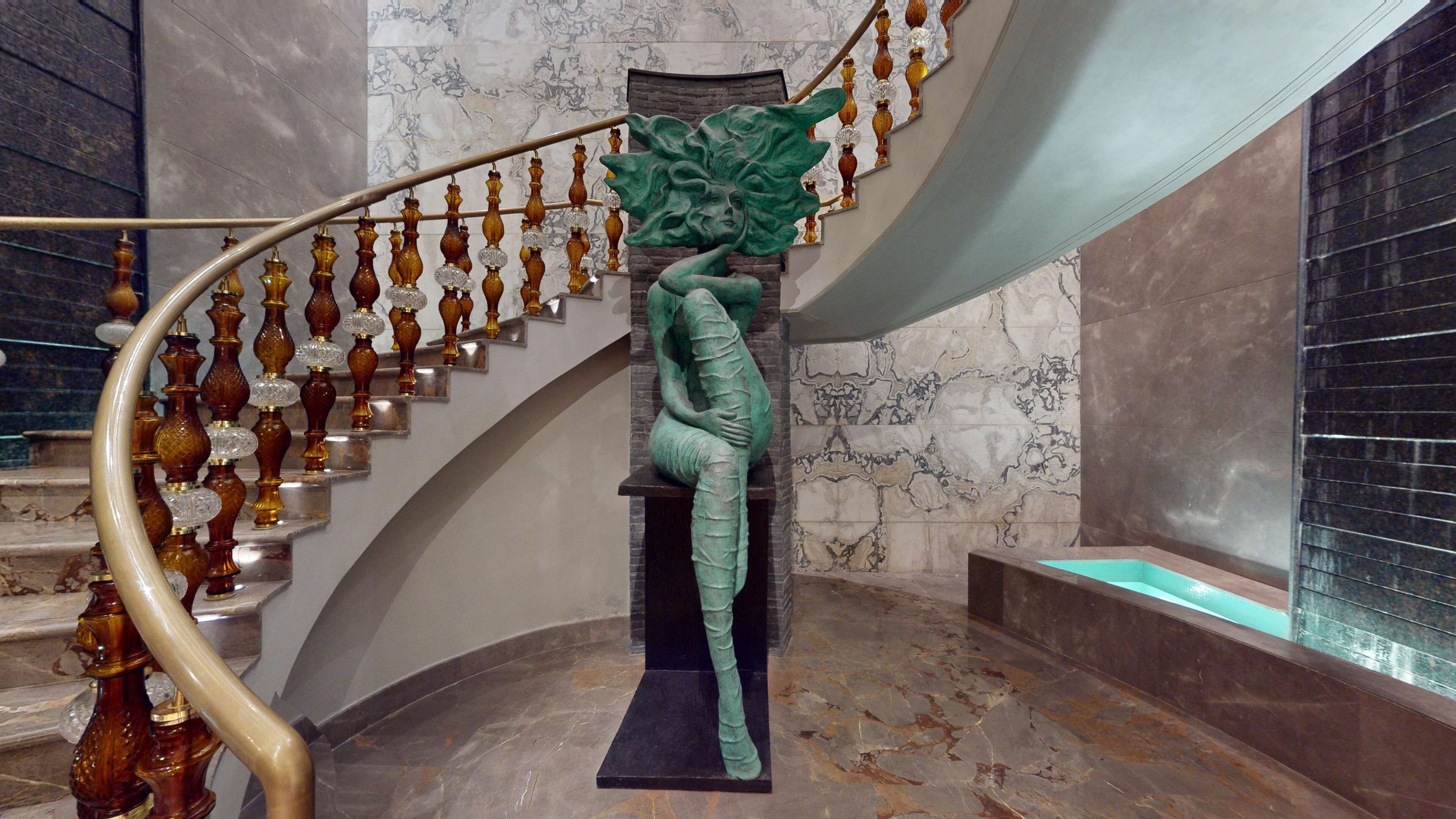 A staircase with a green sculpture, marble walls, and a curved handrail.