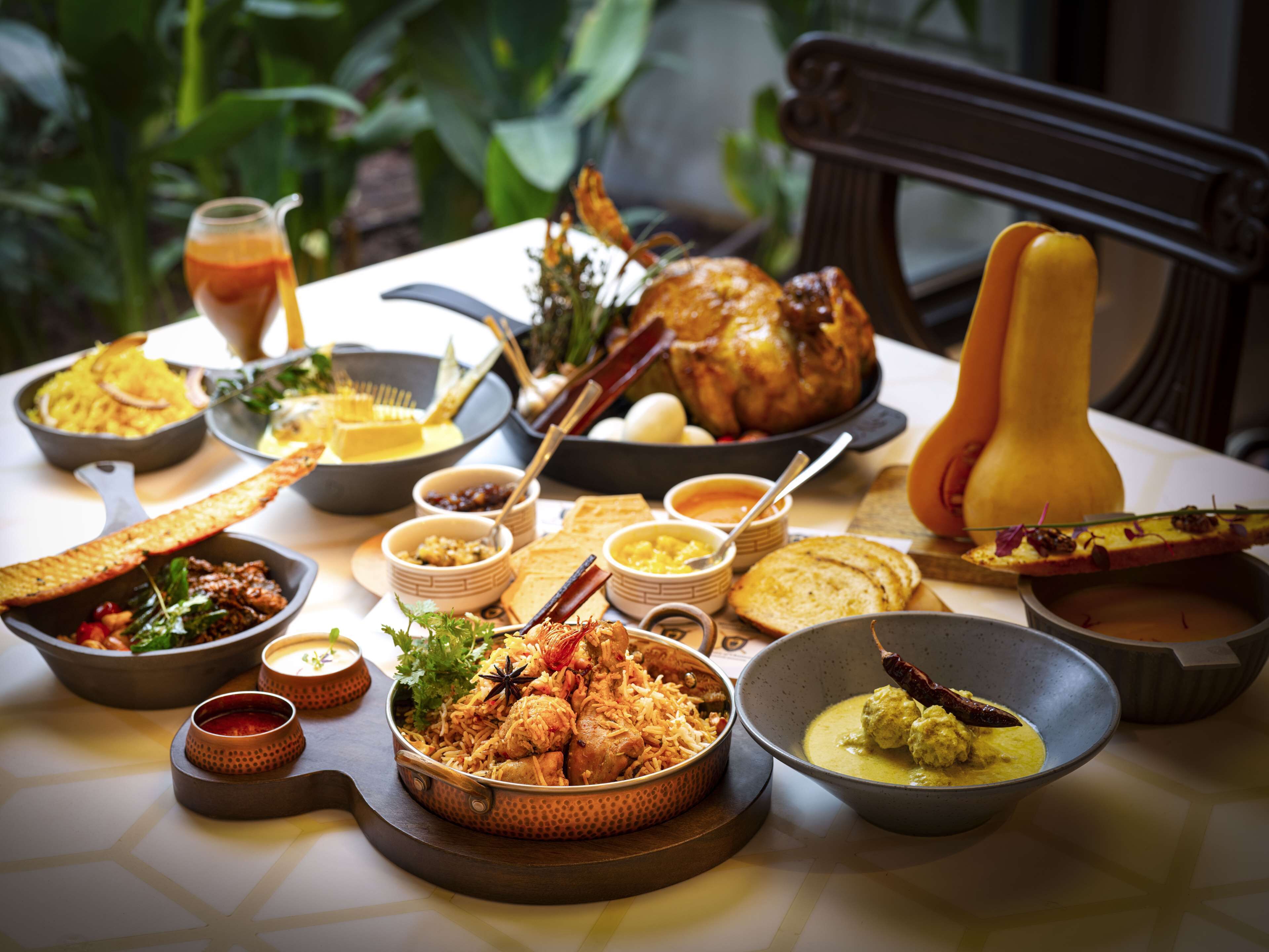 A table set with various dishes including a roasted chicken, rice, bread, and multiple small bowls of sauces and sides.