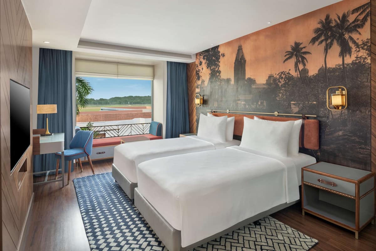 A hotel room with two beds, a desk, a chair, a TV, and a balcony with a view.