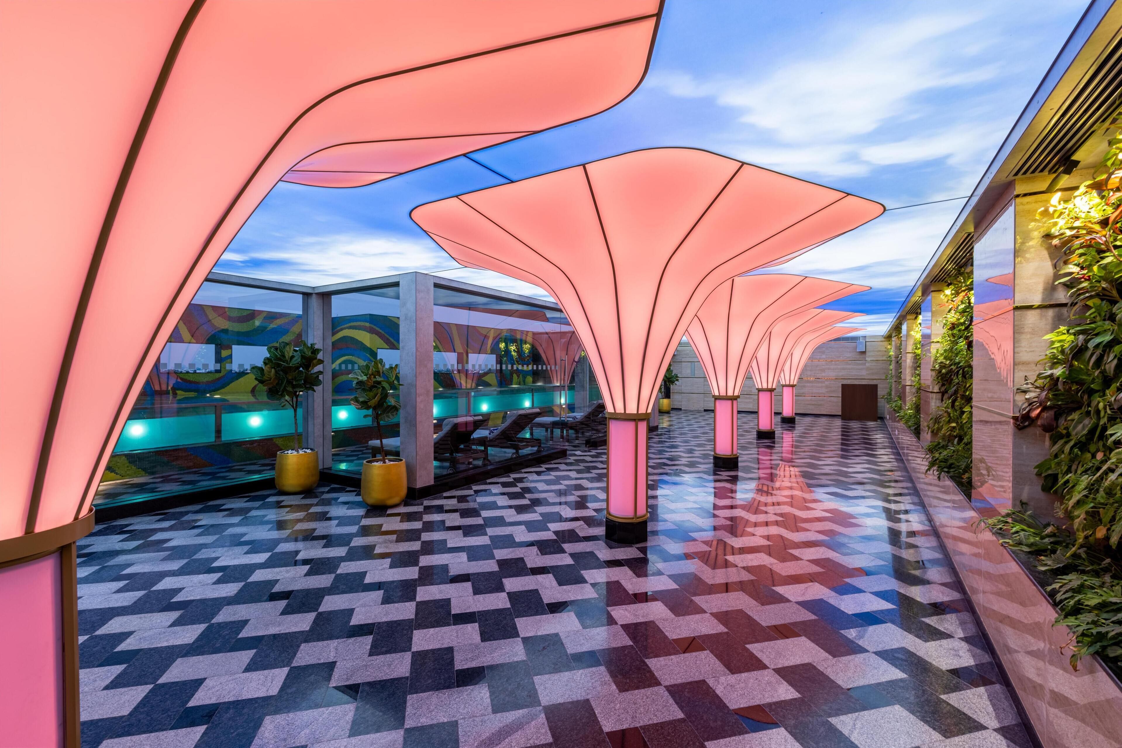 A corridor with a patterned floor, pink canopy structures, and a view of a building with a colorful mural.
