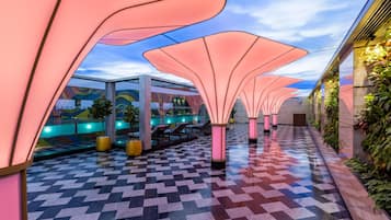 A corridor with a patterned floor, pink canopy structures, and a view of a building with a colorful mural.
