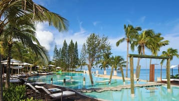 A resort pool area with lounge chairs, palm trees, and a wooden deck.