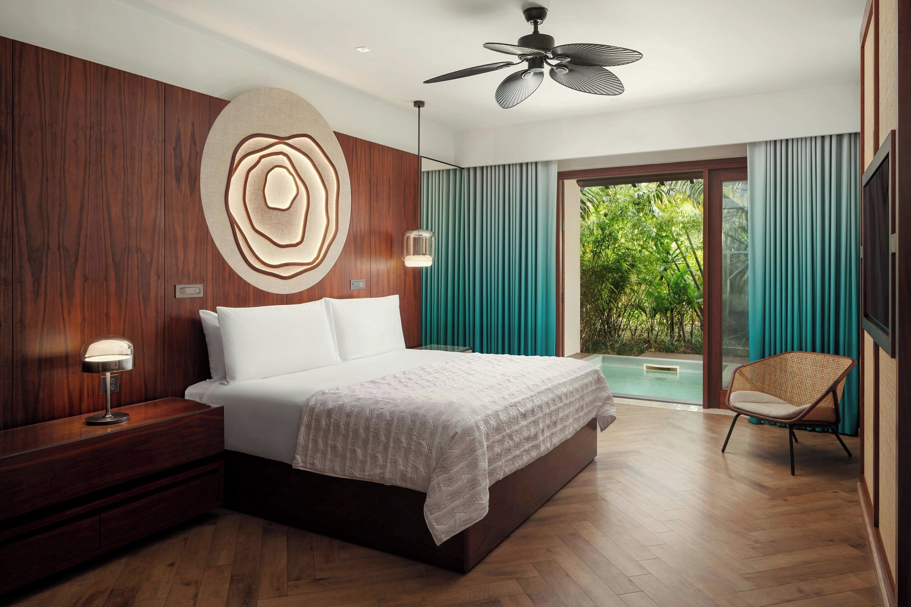 Een moderne slaapkamer met een groot bed, een plafondventilator, een nachtkastje, een stoel en uitzicht op een zwembad.