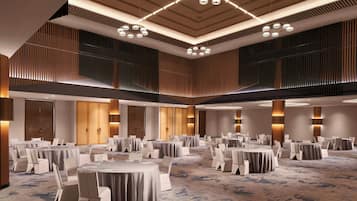 Un amplio salón de banquetes con mesas redondas, sillas blancas y un techo alto con luminarias modernas.