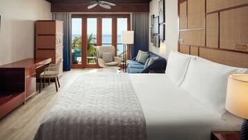 Habitación de hotel con cama, escritorio, silla, sofá, lámpara y vista al océano.