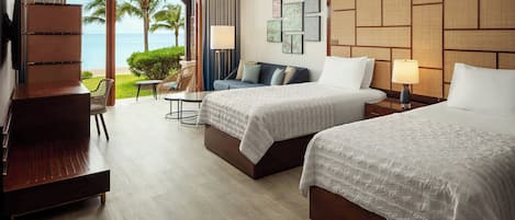 A hotel room with two beds, a desk, a chair, and a balcony with a view of the ocean.