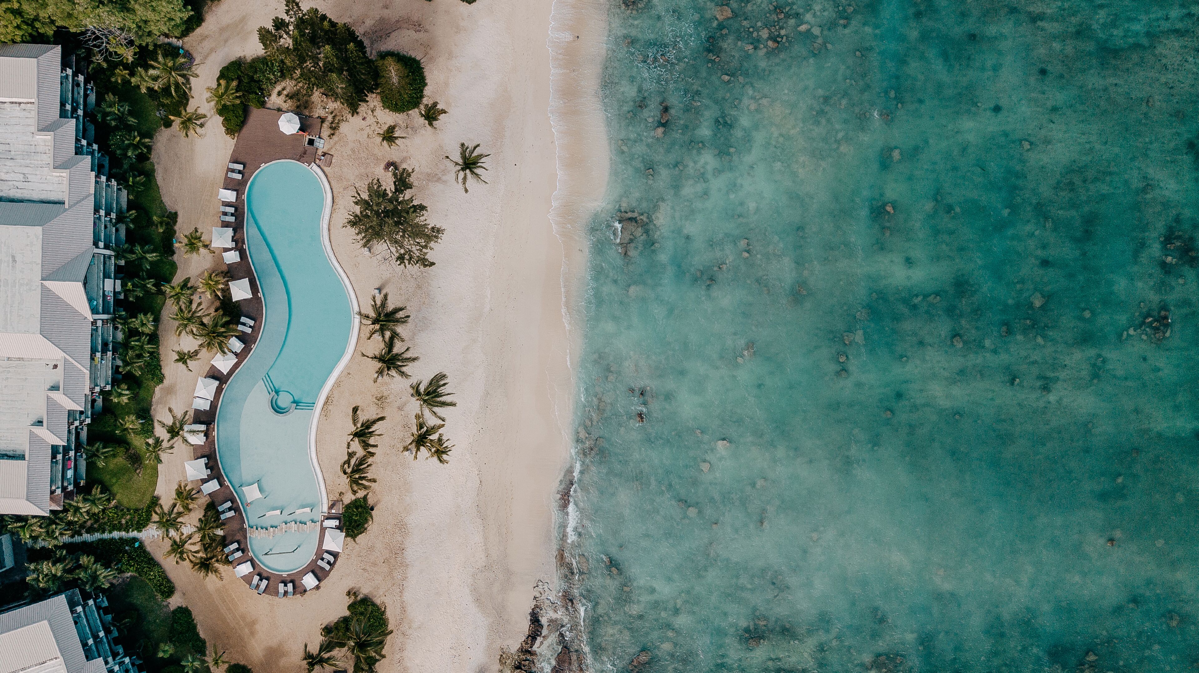 An aerial view of a resort with a swimming pool, beach, and palm trees.